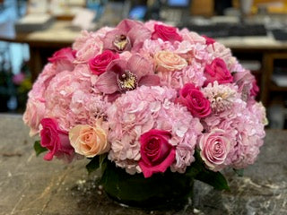 
                    
                      A floral arrangement featuring pink hydrangea, pink roses, hyacinth and orchid heads in a low cylinder vase. - Jerome Florists NYC
                    
                  