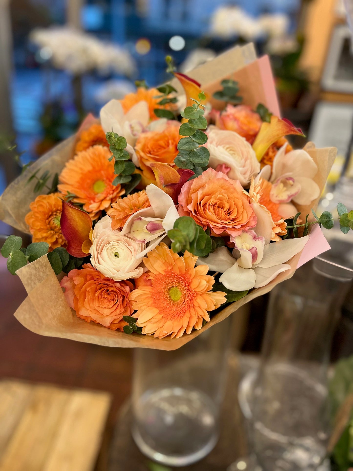 
                    
                      Orange pink roses, gerbera daisy, dahlias, cymbidium orchid heads, eucalyptus and ranunculus sunrise bouquet – Jerome Florists NYC
                    
                  