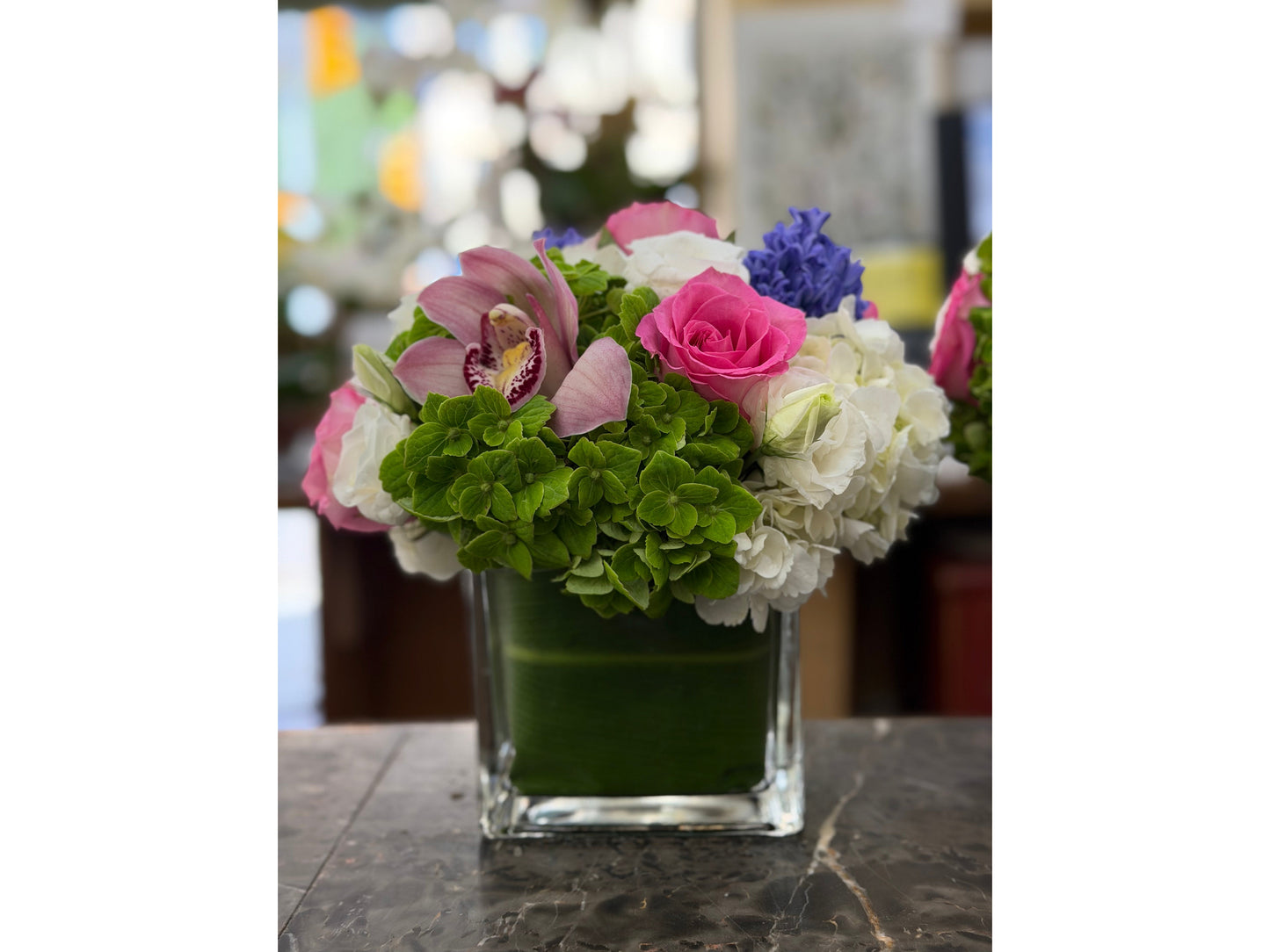 
                    
                      Close view of Eliana on dark veined marble: green hydrangea in front, hot pink rose, speckled pale pink cymbidium orchid
                    
                  